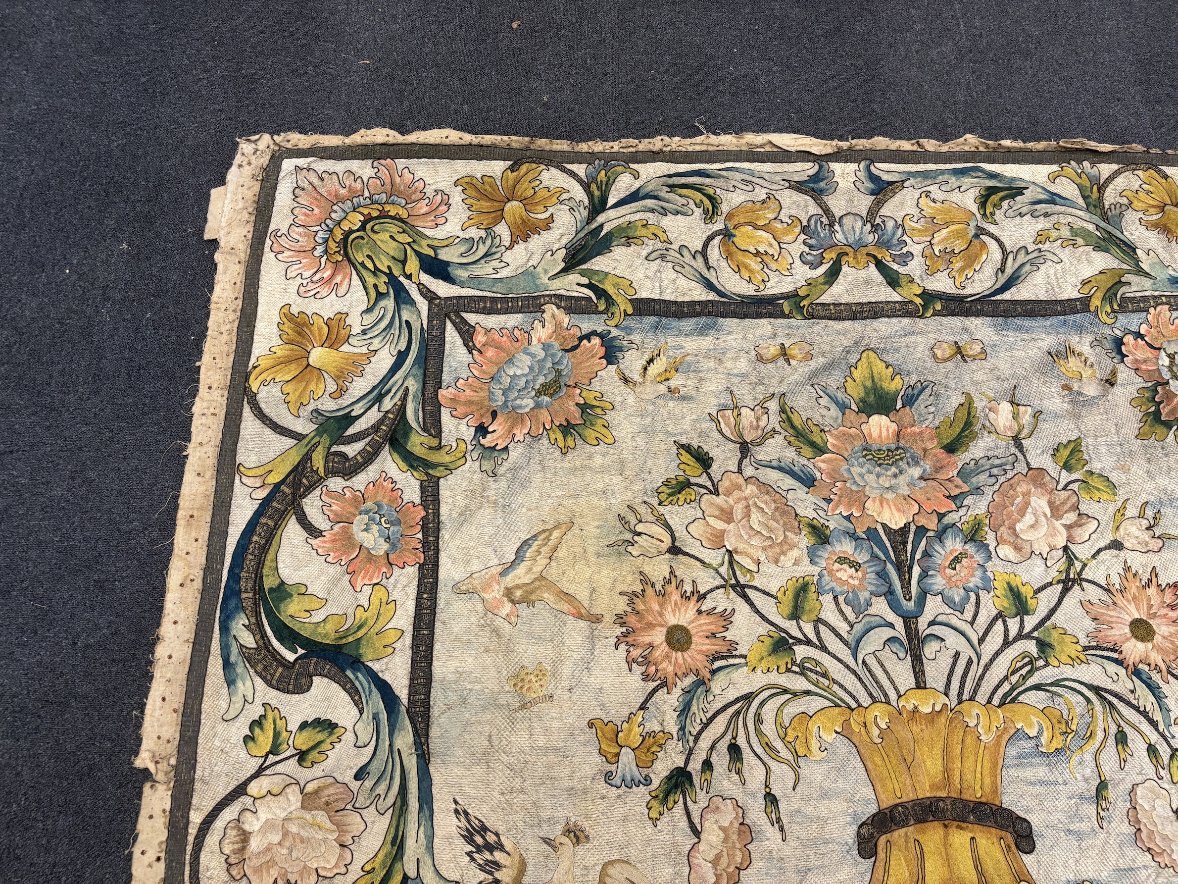 A large early 18th century possibly French polychrome and gold metallic silk embroidered wall hanging, with scrolling vine and floral border. The central motifs embroidered with an elaborate metallic thread cartouche fra